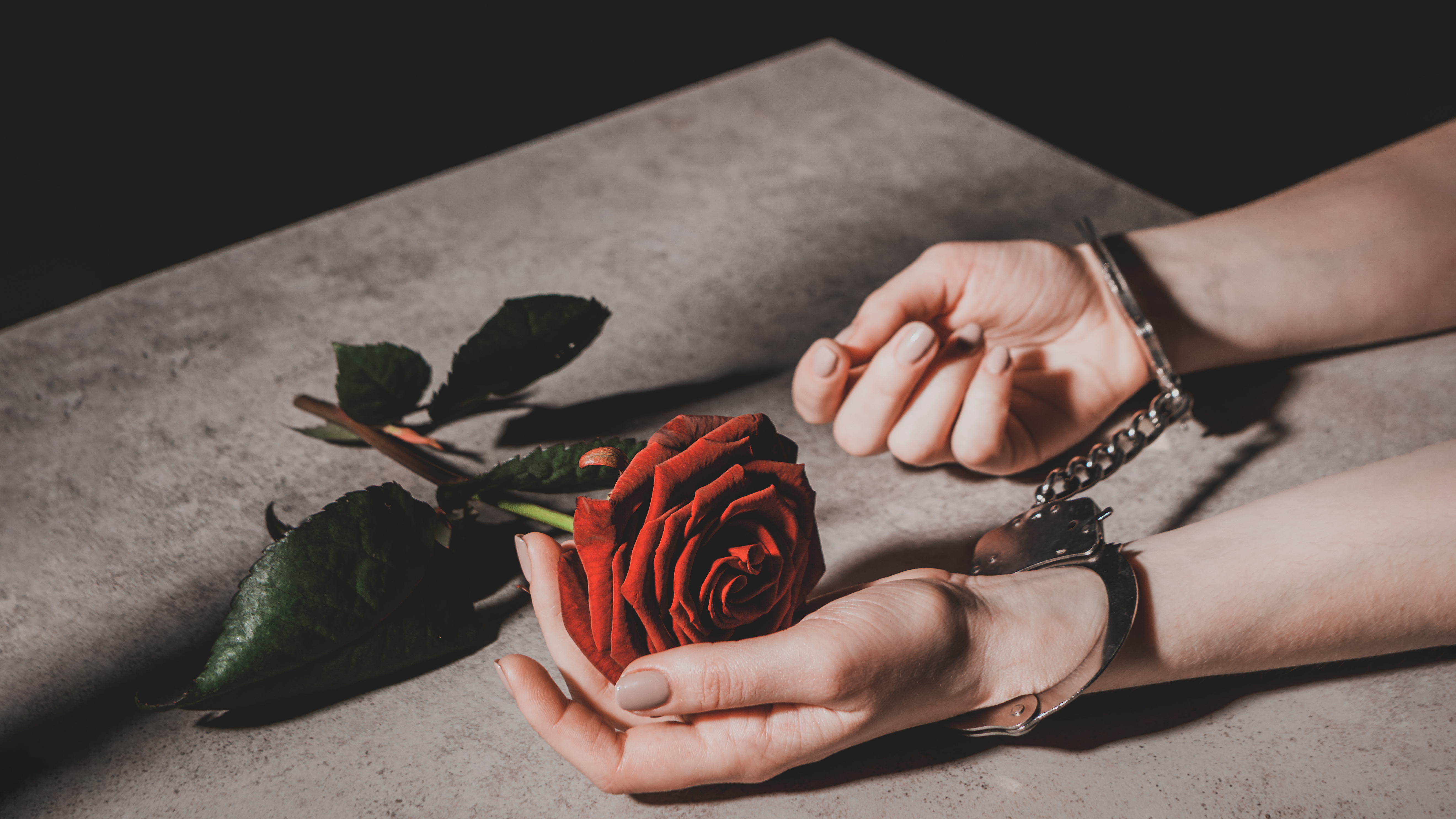 Picture of a woman in handcuffs caressing a red rose.